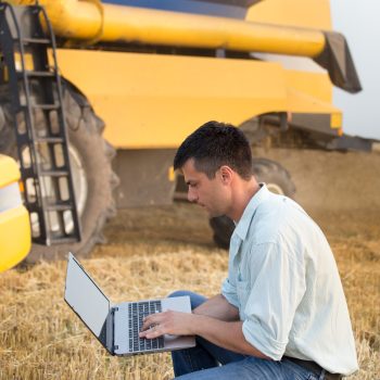 Engineer with laptop with combine harvester Young engineer with laptop standing in front of combine harvester in field